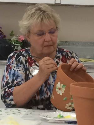 Woman painting floral designs on a terracotta pot indoors.