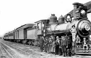 Vintage steam locomotive with passengers posing beside it.